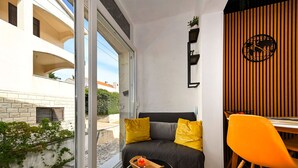 A modern living room with a sofa, a dining table, and a chair. There is a window with a view of a building and greenery outside. - DaLaPaDo by Interhome (Zadar)