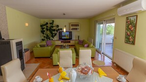 A living room with a television, green sofas, a coffee table, and a dining area with a table set for breakfast. - Green Oasis by Interhome (Imotski)