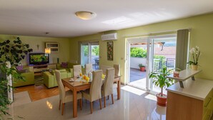 A modern living room with a dining area, a flat-screen TV, and a balcony with potted plants. - Green Oasis by Interhome (Imotski)