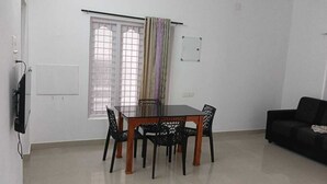 Ein Essbereich mit Tisch und Stühlen, einer schwarzen Couch, einem Fenster mit Vorhängen und einer wandmontierten Steckdose.