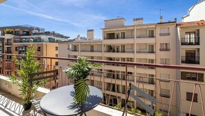 Ein Balkon mit Tisch und Stühlen, einem Blumentopf und Blick auf mehrstöckige Gebäude.