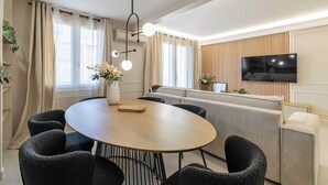 Ein modernes Wohnzimmer mit einem runden Holztisch, schwarzen Polsterstühlen, einem beigen Sofa und einem an der Wand befestigten Flachbildfernseher.