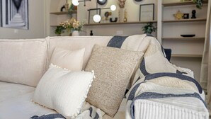 Ein Wohnzimmer mit einer Couch, die mit verschiedenen Kissen geschmückt ist, einer Wandleuchte und Regalen mit Dekoration.