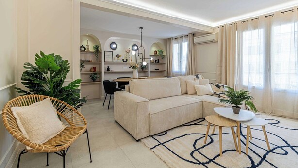 Ein Wohnzimmer mit einer Couch, einem Korbstuhl, einem kleinen Tisch und einer großen Topfpflanze.