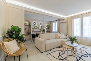Ein Wohnzimmer mit einer Couch, einem Korbstuhl, einem kleinen Tisch und einer großen Topfpflanze.