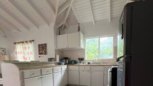 A kitchen with white cabinets, a window with a view of greenery, and a refrigerator. - The Tree House - by ZenBreak (Workmans)
