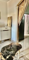 Una habitación con una mesa de mármol, un armario blanco, una obra de arte de madera, una columna y un refrigerador.