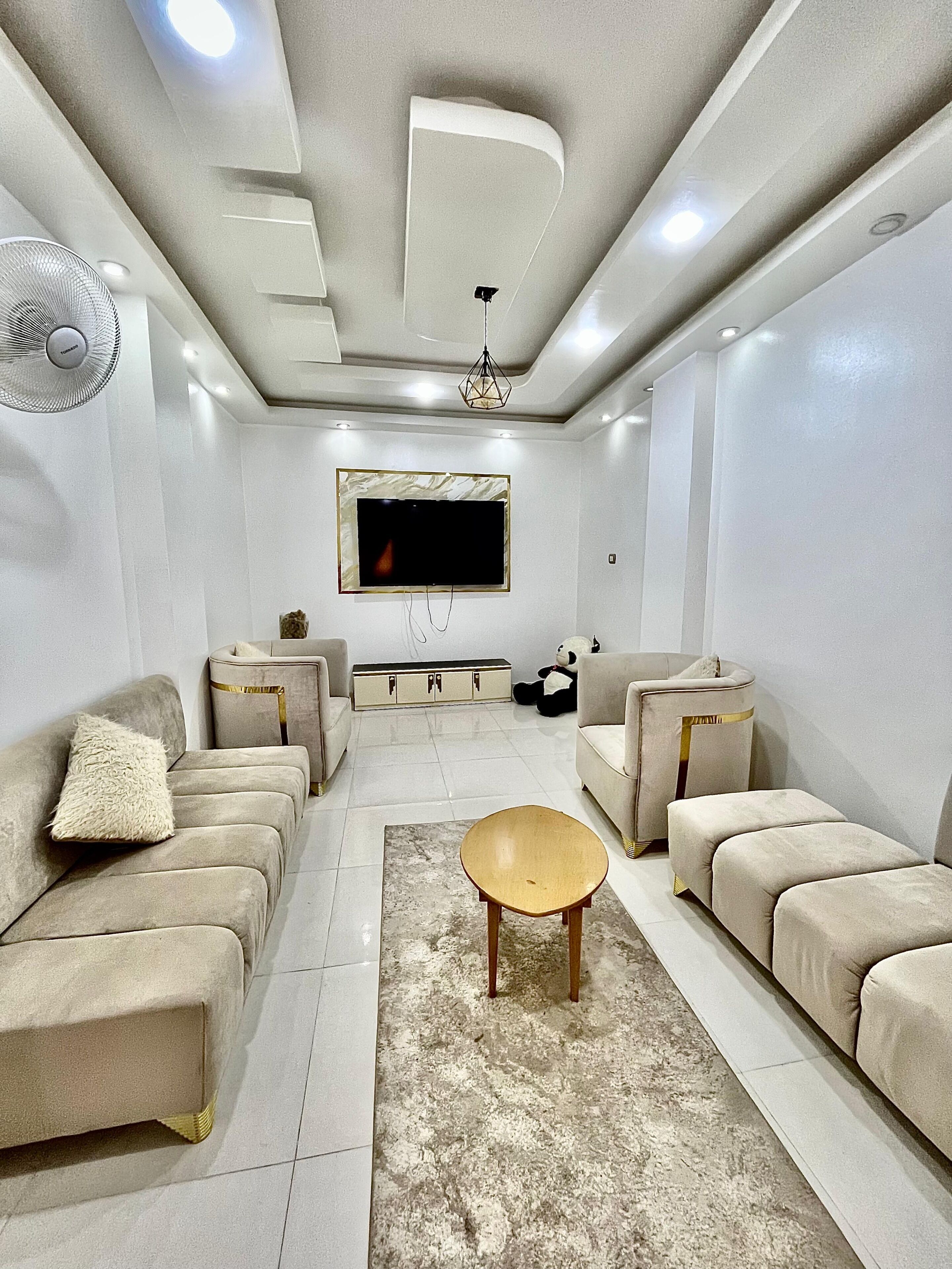 Una sala de estar moderna con sofás, una mesa de centro, un televisor y un ventilador de techo.