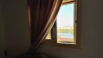 A room with a bed, a window with curtains, and a view of a landscape.