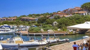 A marina with boats docked, a clear sky, and houses in the background. - Porto Rotondo - Appartamento in Centro, 8 Minuti Da Spiaggia Ira (Olbia)