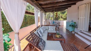 A covered outdoor seating area with a wooden bench, a sofa, and a table. - Porto Rotondo - Appartamento in Centro, 8 Minuti Da Spiaggia Ira (Olbia)