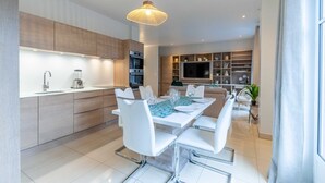 A modern kitchen with white cabinetry, a dining area with a white table set for four, and a large window providing natural light.