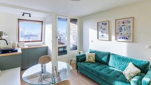 Uma sala de estar moderna com um sofá verde, uma mesa de vidro e vista para a cidade através de uma janela ampla.
