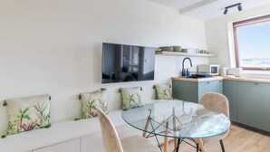 Uma cozinha moderna com televisão de tela plana, uma área de refeições com mesa e cadeiras de vidro, e uma janela com vista.