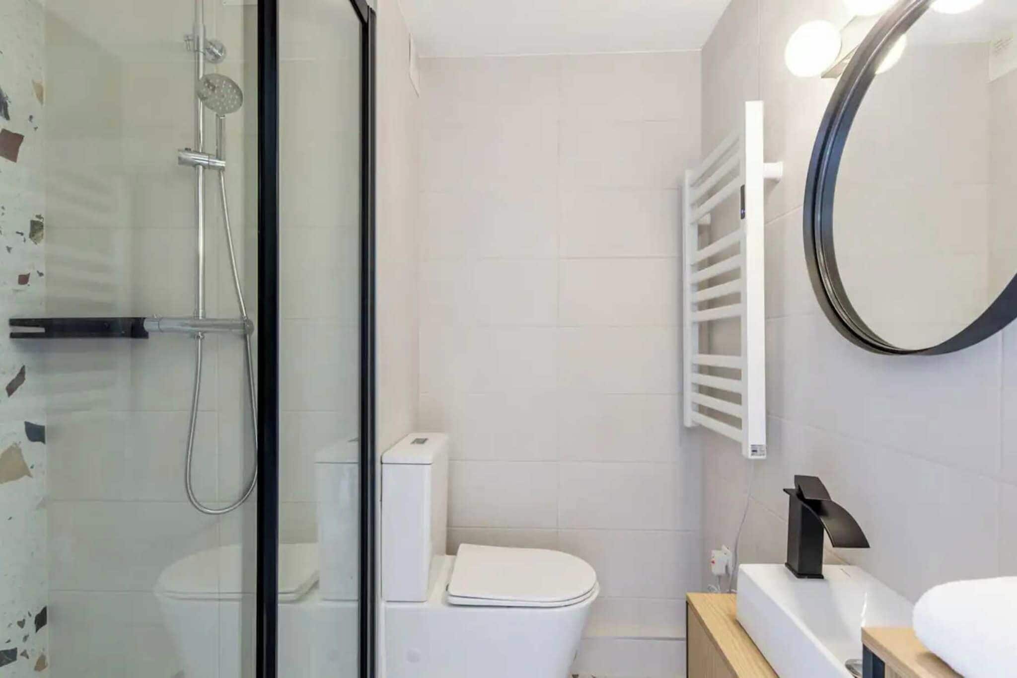 Un baño moderno con ducha de vidrio, inodoro blanco y espejo redondo.