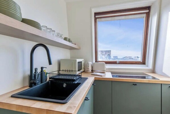 Una cocina compacta con un lavamanos negro, una ventana con vistas y un microondas en la encimera.