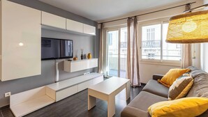 Un soggiorno moderno con divano, tavolino, televisore a parete e un balcone con tende.