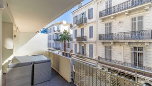 Un balcone con mobili in vimini, una palma e vista sui palazzi vicini.