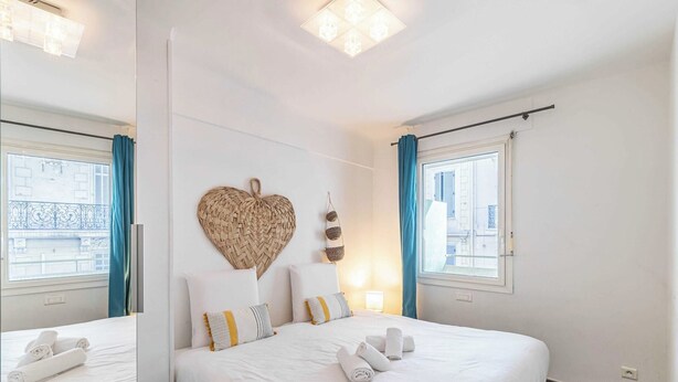 Una camera d'albergo con un letto grande, un decoro a forma di cuore sulla parete e vista sulla città dalle finestre.