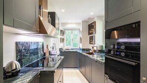 Une cuisine moderne avec des meubles de couleur sombre, un plan de travail en marbre et des appareils électroménagers en acier inoxydable.