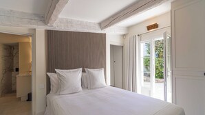 Une chambre avec un grand lit, une tête de lit en lattes de bois et une vue sur la verdure par une porte.