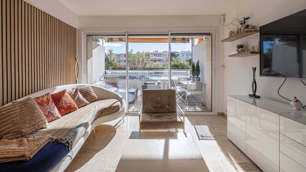 A modern living room with a sofa, armchair, and a glass door leading to an outdoor balcony.