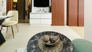 A modern living room with a flat-screen TV, white cabinets, a round marble coffee table, and a green sofa. - Saint Honore & Saint Dominique (Iloilo)