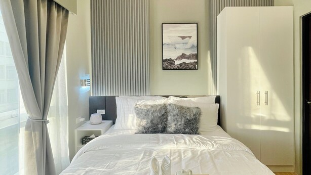 A modern hotel room with a neatly made bed, a bedside table with a lamp, a large wardrobe, and a framed picture on the wall. - Saint Honore & Saint Dominique (Iloilo)