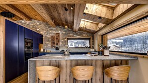 Une cuisine moderne avec un mur d’accent en pierre, des poutres en bois au plafond et une grande fenêtre donnant sur un paysage enneigé.