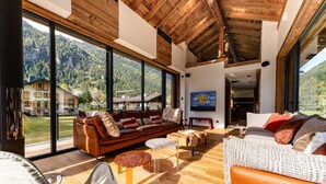 A spacious living area with a large wooden ceiling, a leather sofa, and a white woven sofa. - Serviced Luxury Chalet with 10m Indoor Pool (Chamonix-Mont-Blanc)