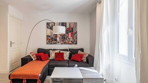 A modern living room with a grey sofa, red cushions, a white coffee table, and a large cityscape painting on the wall. - Beautiful apartment - Croisette Gray Albion (Cannes)