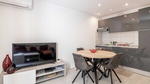 A modern kitchen with grey cabinets, a built-in oven, and a dining area with a round table and chairs. - Beautiful apartment - Croisette Gray Albion (Cannes)