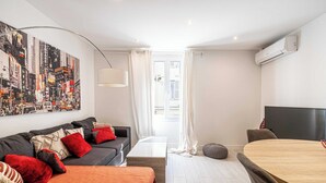 A modern living room with a large cityscape painting, a grey sofa with red and black cushions, a wooden coffee table, and a round dining table with grey chairs. - Beautiful apartment - Croisette Gray Albion (Cannes)