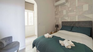 Ein Schlafzimmer mit einem großen Bett, einem Nachttisch, einer Lampe und einem Sessel.
