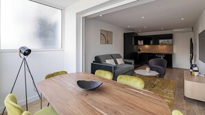 Uma sala de estar moderna com uma mesa de jantar de madeira, cadeiras amarelas, um sofá cinza e uma área de cozinha ao fundo.