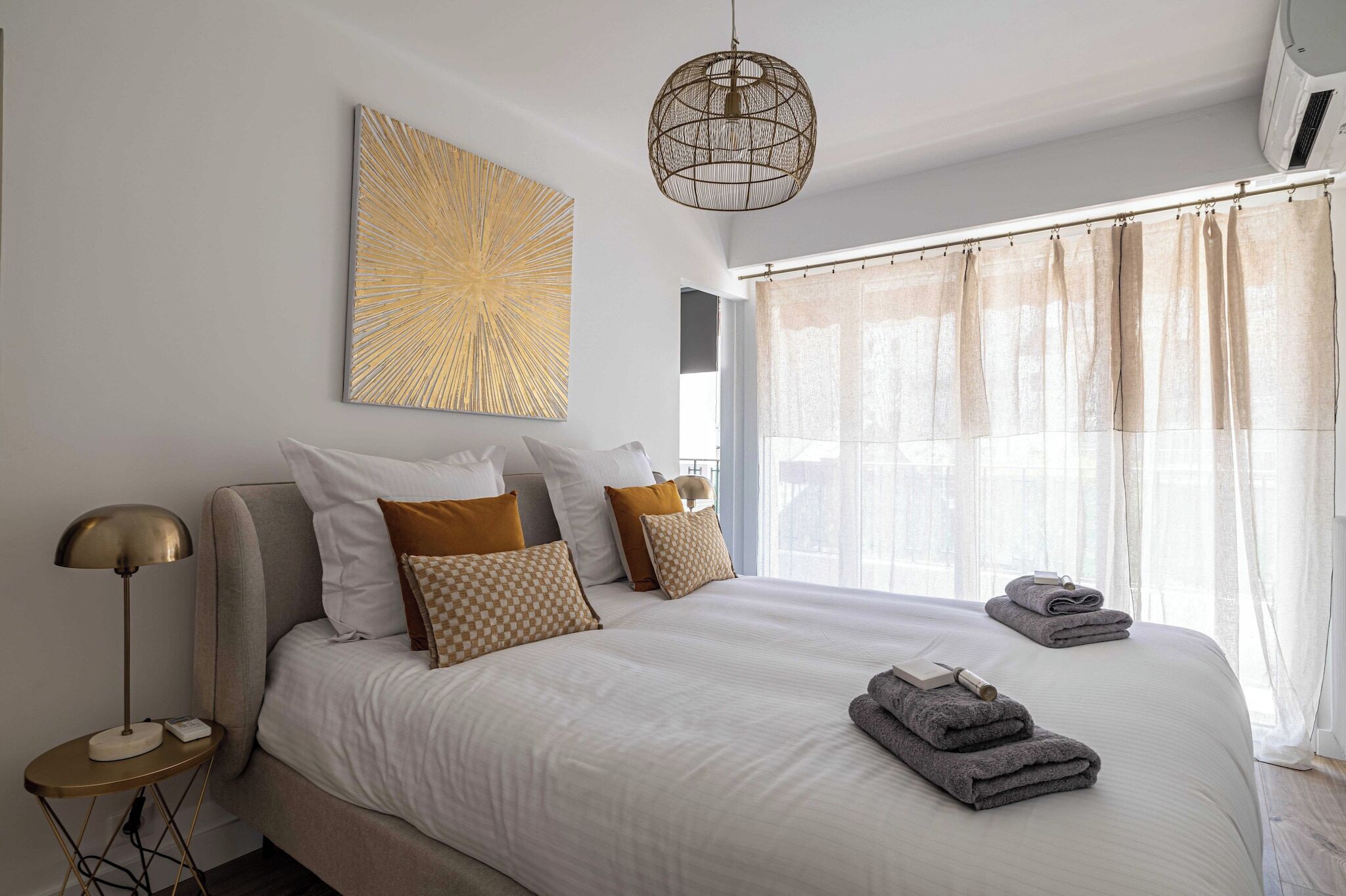 A neatly made bed with white linens, a large abstract artwork above it, and a hanging light fixture.