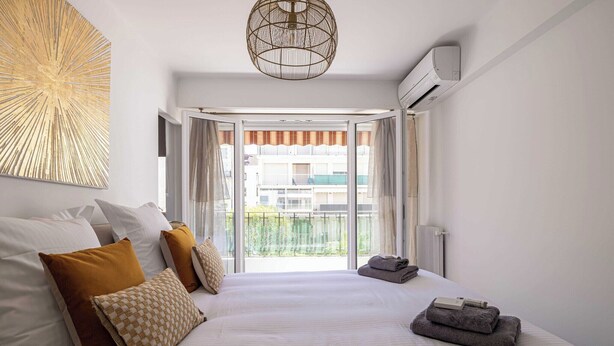 Quarto de hotel moderno com uma cama grande, vista para a cidade e ventilador de teto.