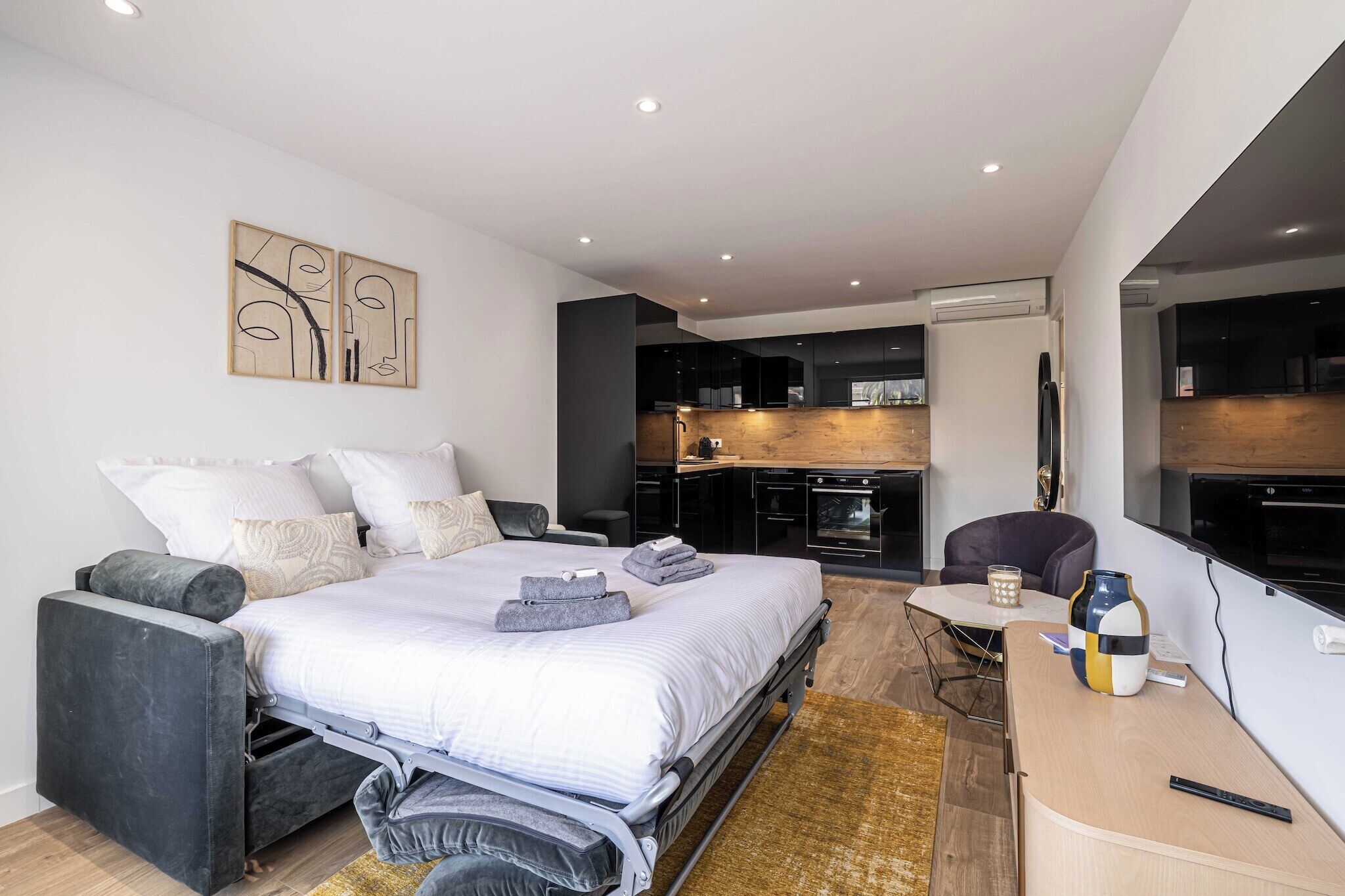 A modern bedroom with a bed, bedside table, and a small kitchenette area.