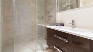Un baño moderno con cabina de ducha de vidrio, un lavamanos blanco y un espejo grande.