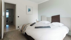 Una cama bien hecha con edredón blanco, un plaid gris y un cuadro en la pared.