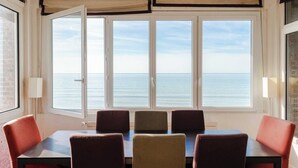 Une pièce dotée d’une grande fenêtre donnant sur la mer, d’une table avec des chaises et d’une lampe sur le côté.