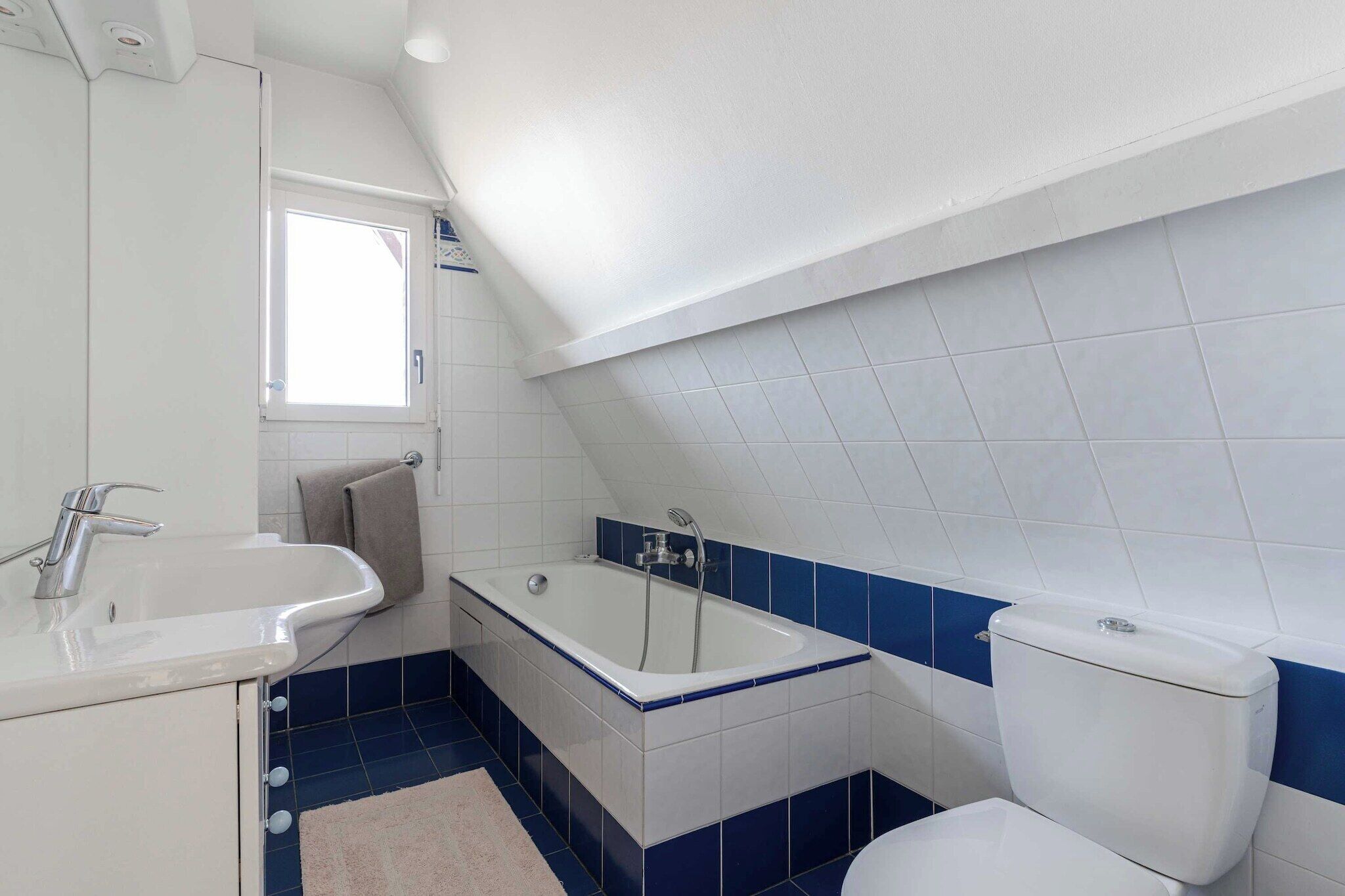 A bathroom with a bathtub, toilet, sink, and a window.