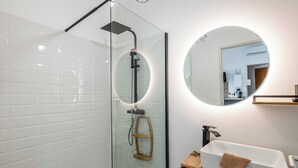Een moderne badkamer met een douchecabine van glas, een witte wastafel met houten dienblad en een ronde spiegel.