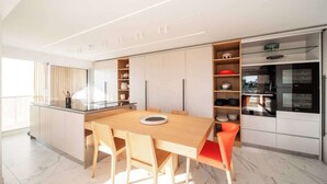 A modern kitchen with a central island, built-in appliances, and a dining area with a red chair. - Sumptuous terrace apartment - Cannes - Sea view (Cannes)