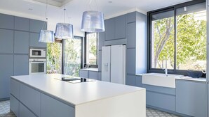Una cocina moderna con una isla grande, electrodomésticos integrados y amplios ventanales con vistas a la vegetación.