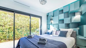 Un dormitorio moderno con una cama grande, vistas a la vegetación a través de una puerta corrediza y un diseño geométrico en la pared.