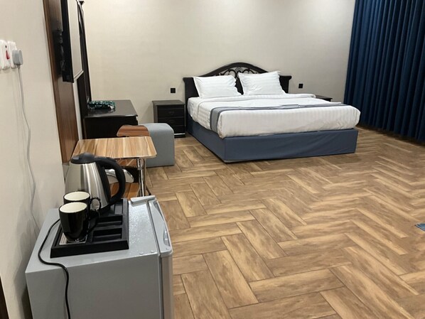Habitación de hotel con cama, escritorio con tetera, silla, mesita y calefactor.