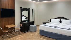 A bedroom with a bed, a dresser, a mirror, a TV, and a folding chair. - AlBaidaa AlSalam branch (Madinah)