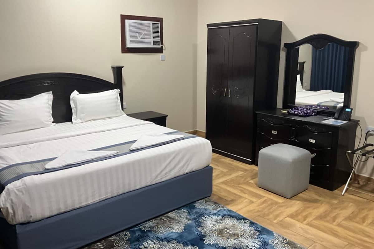 Une chambre à coucher comprenant un lit, une armoire, un bureau avec un miroir et un petit tabouret.