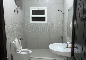 Un baño con inodoro, lavabo, ducha y un ventanal pequeño.